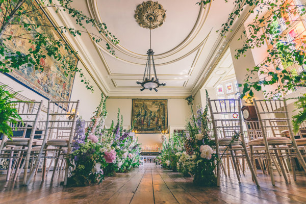 Wild flowers and trees line the aisle of beautiful wedding hall in a stately home mansion house in the cotswolds