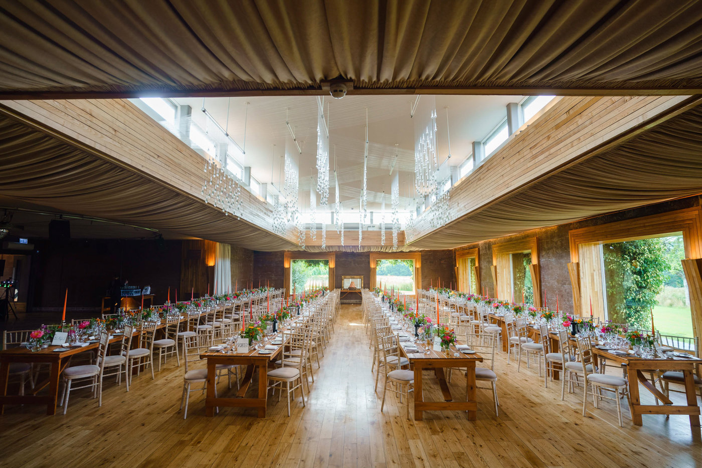 Huge wedding reception for 200 guests with long banqueting tables decorated with pink and orange flowers and candles