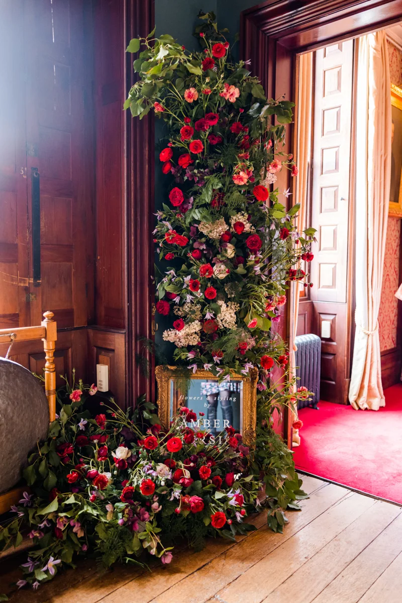 Beautiful bold red flower wall with greenery foliage to match red carpets in mansion house wedding venue elmore court for a wild wedding fair in 2022