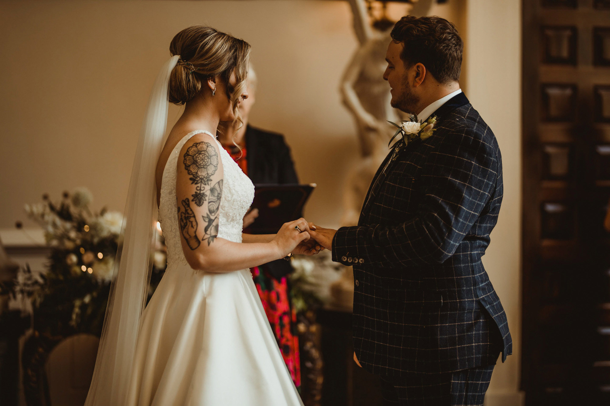 Tattooed bride and groom in tweed suit at their wedding ceremony in stately home