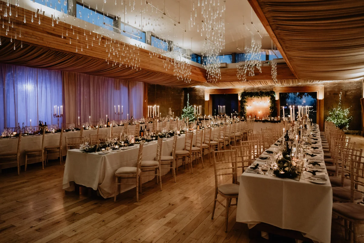 three long wedding reception tables in the Gillyflower at Elmore Court, all candle lit and elegantly decorated