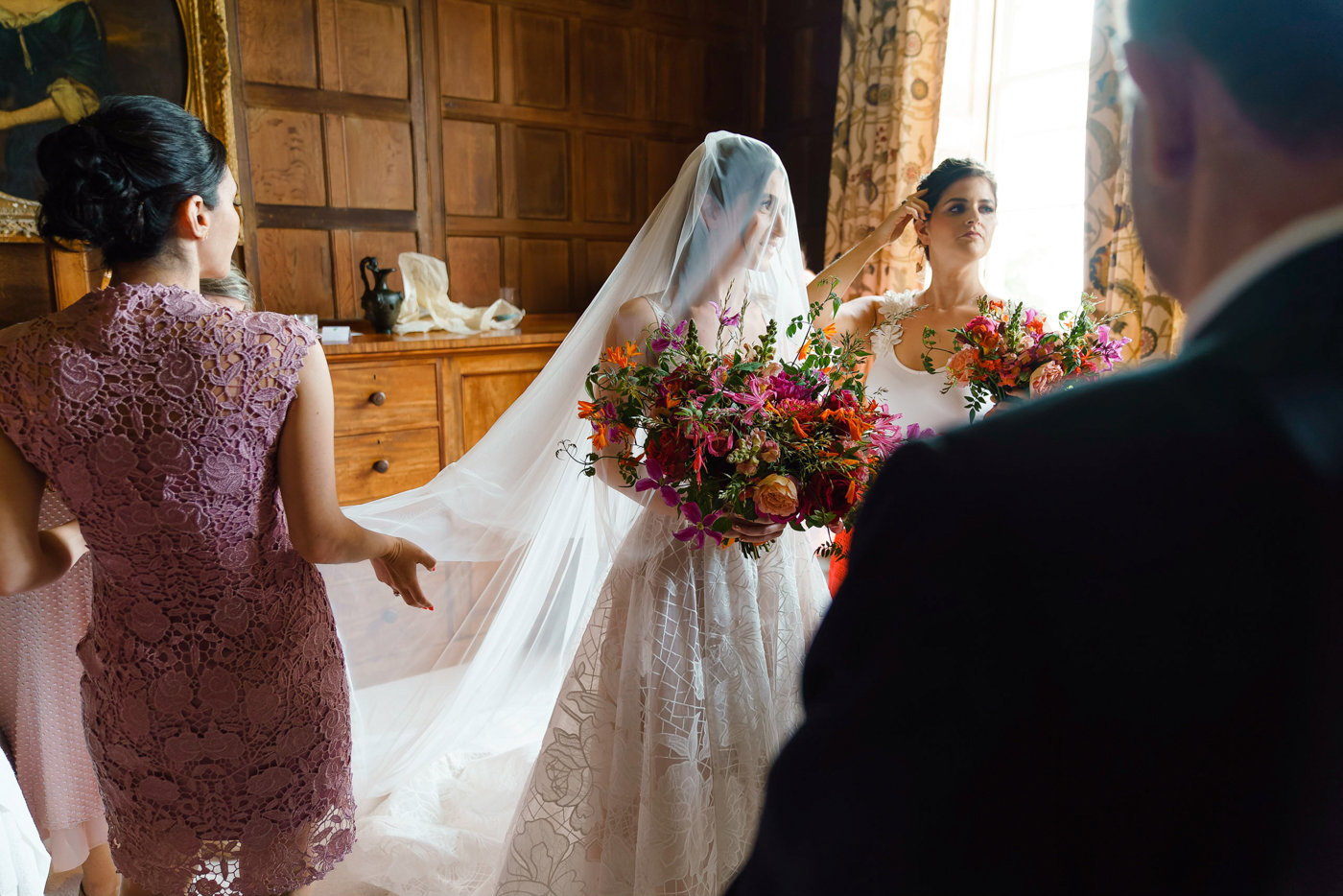 Veiled bride holds huge bright pink and orange statement bouquet of flowers at her bedeken jewish wedding