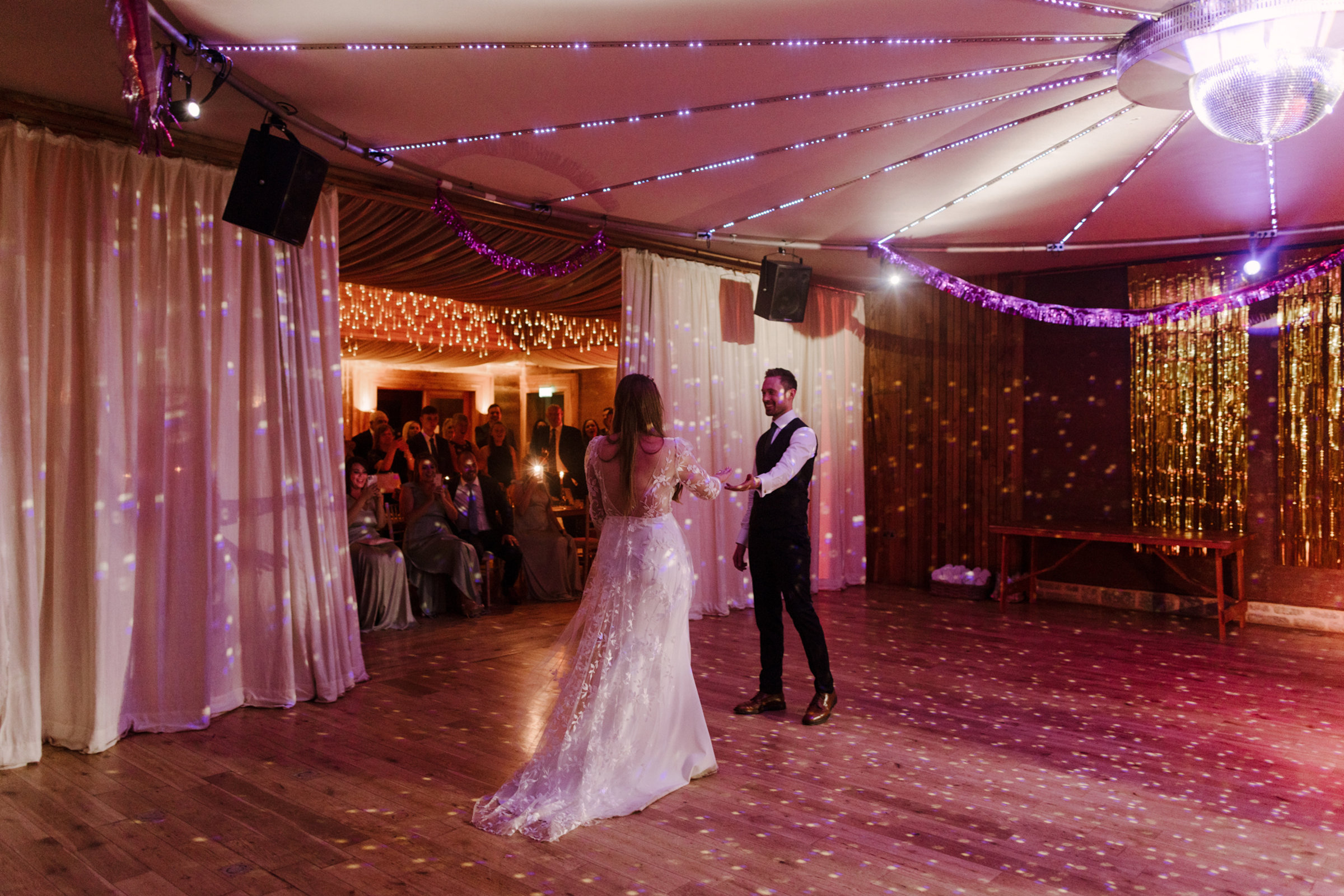 Modern boho luxe couple take their first dance on a pretty pink lit dance floor at eco Cotswolds wedding venue