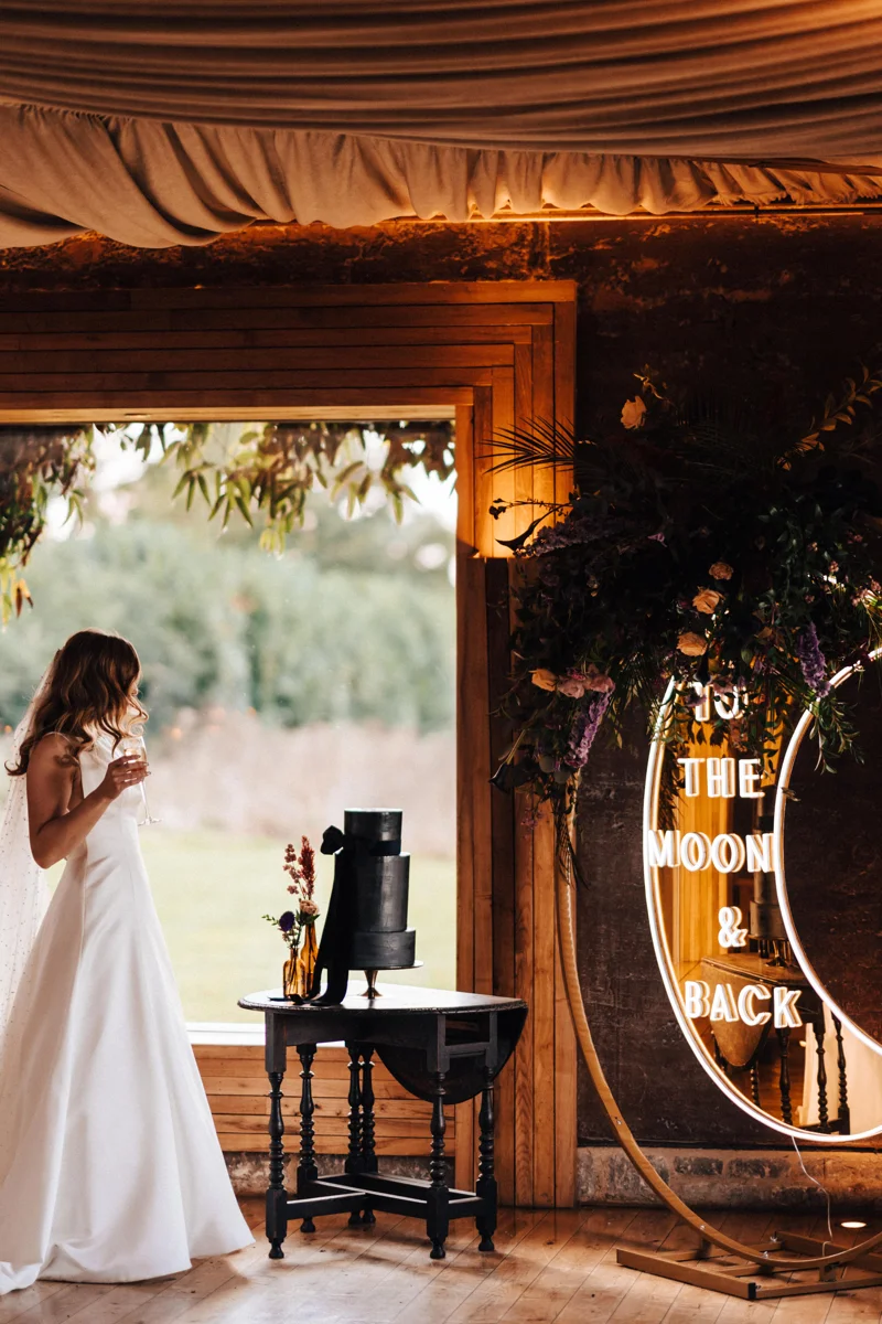 Bride admiring her black wedding cake at celestial wedding with giant to the moon and back sign