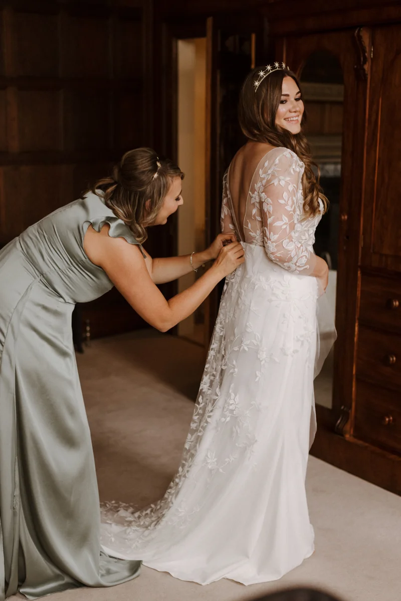 beautiful boho bride getting into her long french lace dress in stately home bedroom