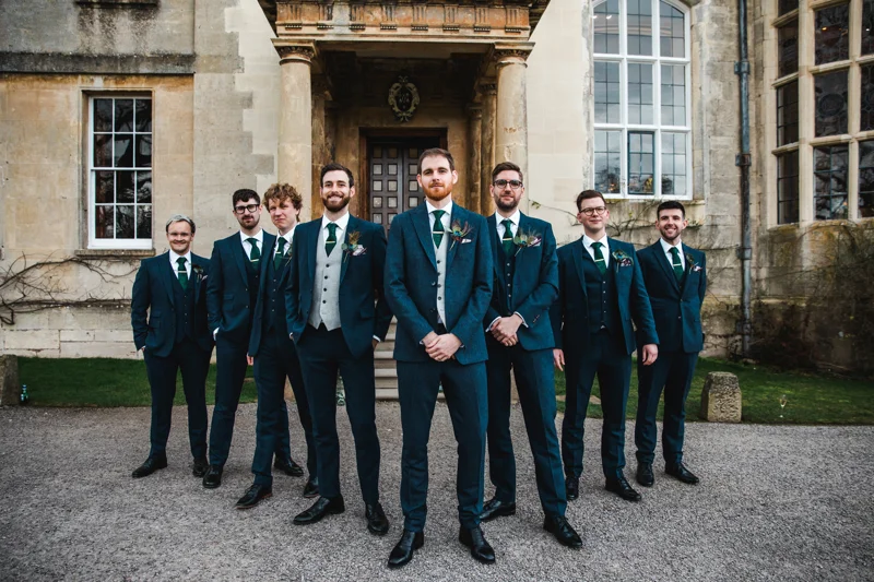 7 smartly dressed Groomsmen stand to attention outside grade 2 listed mansion house weekend wedding venue