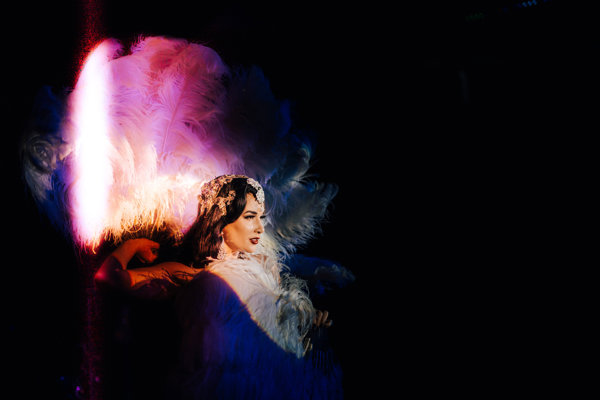 Burlesque star Missy fatale sparkles with fans of beautiful feathers lit up in pink at cabaret dinner pop up at cotswolds wedding venue elmore court