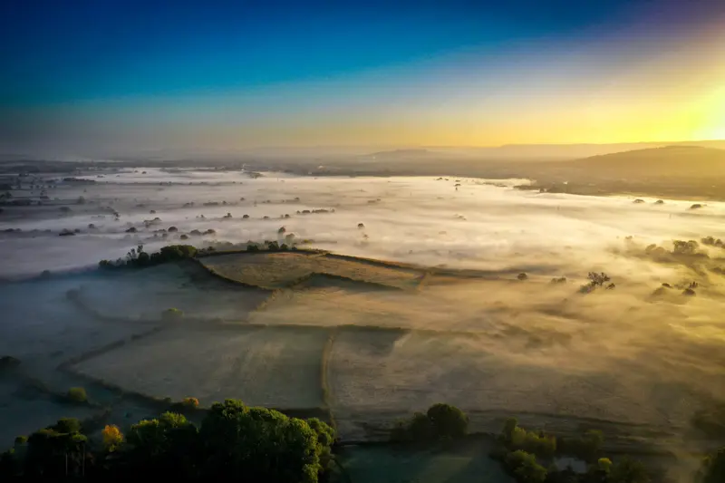 Aerial view of rewilding land which you can now stay within in a treehouse at sunrise covered in fog in the beautiful Cotswolds countryside estate of Elmore Court