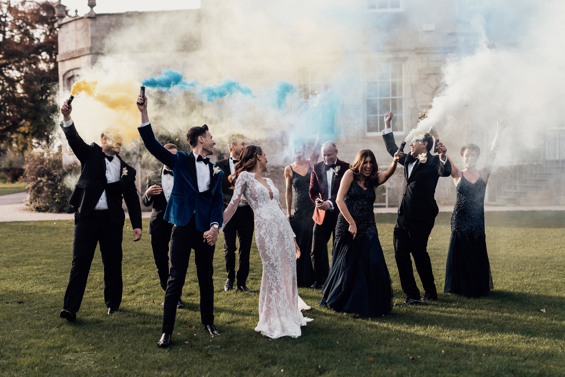 Luxe bride and groom with smoke bomb wedding party in front of stately home elmore court in the cotswolds for a party wedding