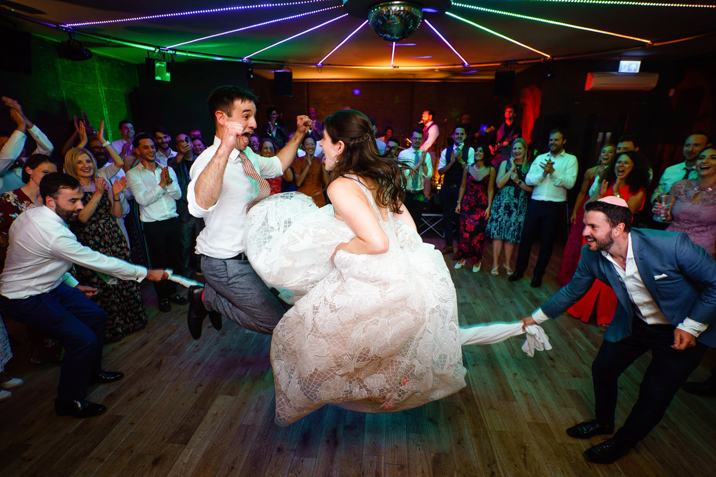 Jewsih wedding party newlywed couple skipping together in rope made of napkins with huge smiles on their faces at party wedding venue elmore court
