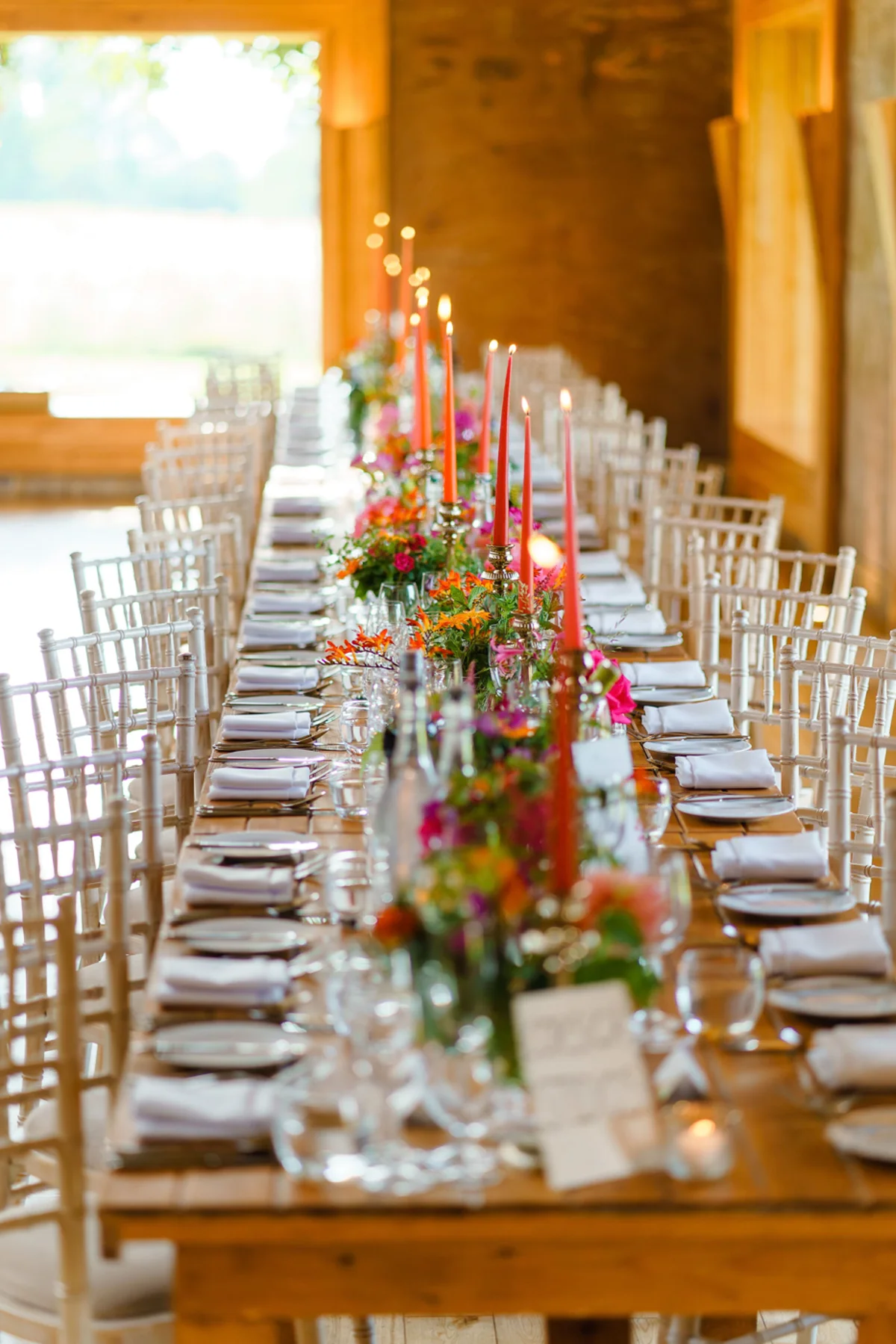 Pink and orange wedding theme reception with flowers and real candles on long wooden tables in The Gillyflower at Elmore Court for a Jewish summer wedding