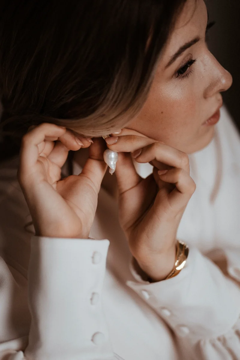Girl with the pearl earring wedding inspiration bride in button cuffs doing up rough pearl earrings