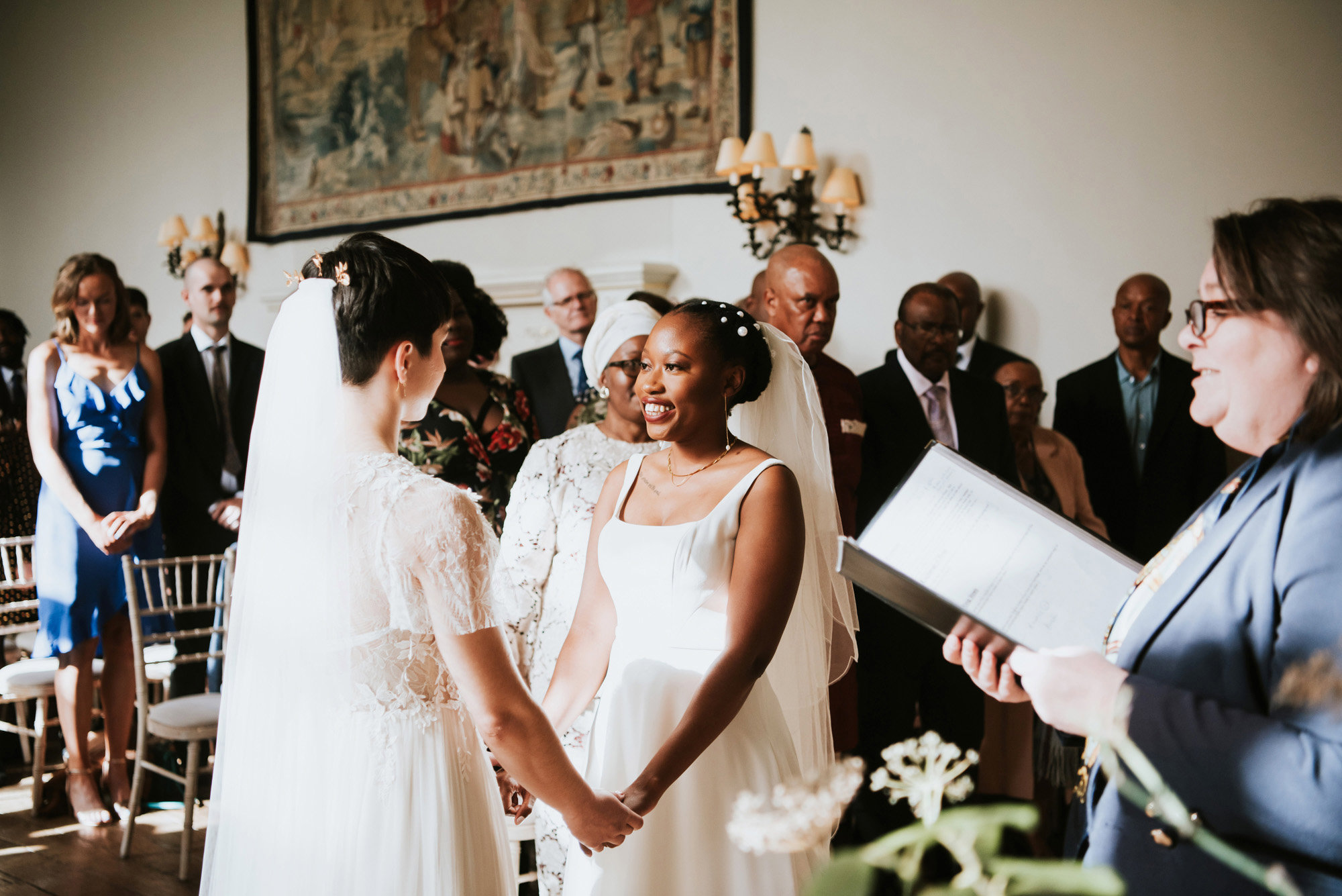 Magical lgbtq wedding ceremony with two brides holding hands saying vows in mansion house hall