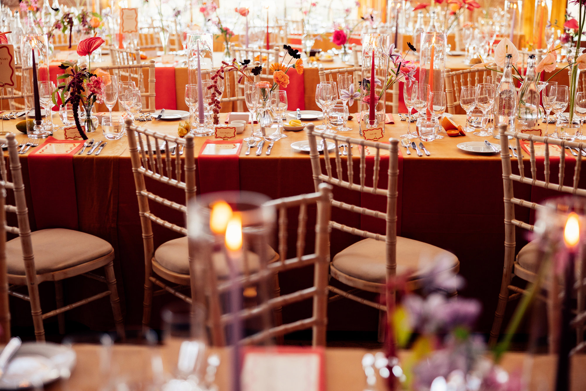 Colourful wedding reception. Orange tables with bright flowers at eco venue in the cotswolds
