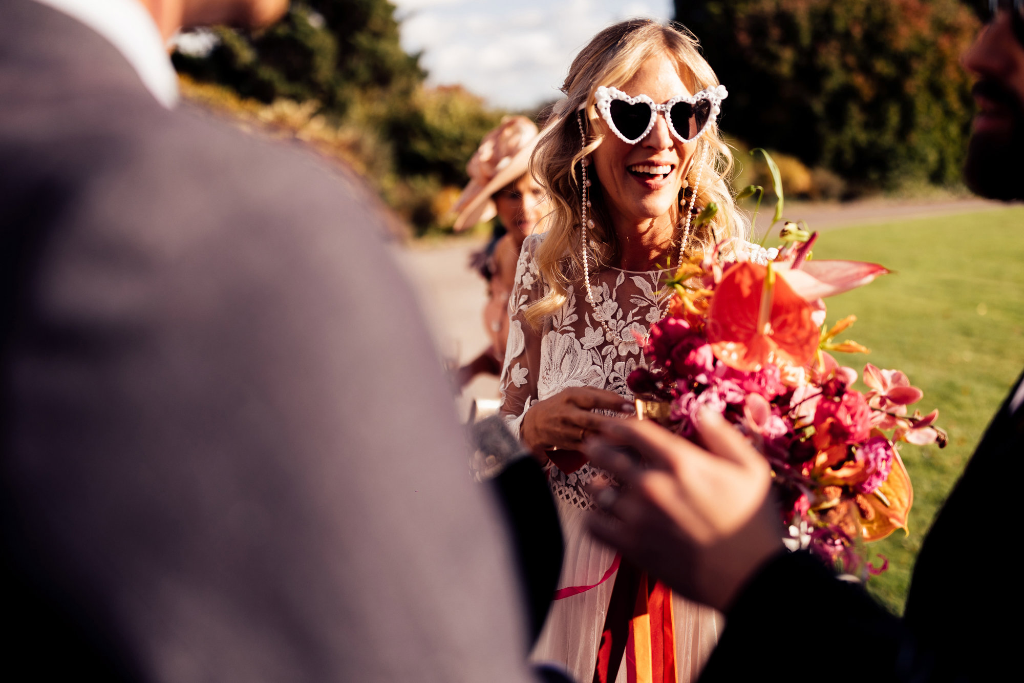 cool bride in heart shaped sunglasses and bright wedding flowers in sunny drinks reception outside elmore court