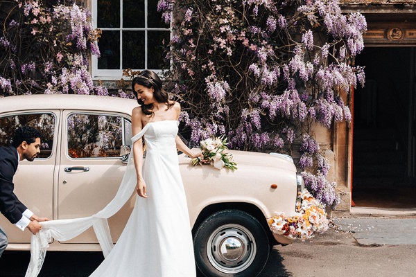 unique wedding car an indian ambassador with flowers decorating the front outside stately home wedding venue elmore court covered in wisteria