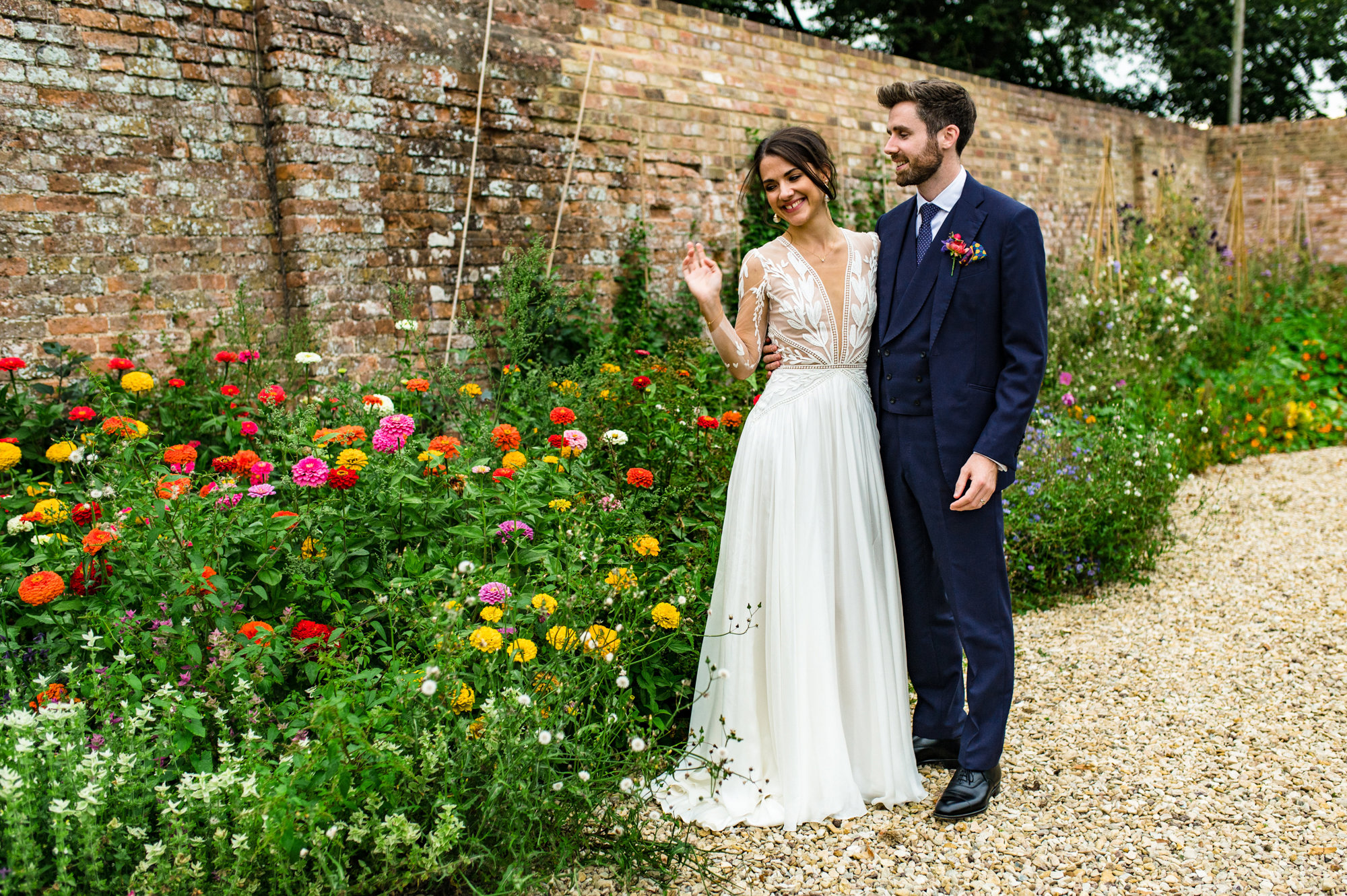 Elegant bride in glamourous french wedding dress stands with her husband next to the flowers in the walled garden at elmore court on their wedding day