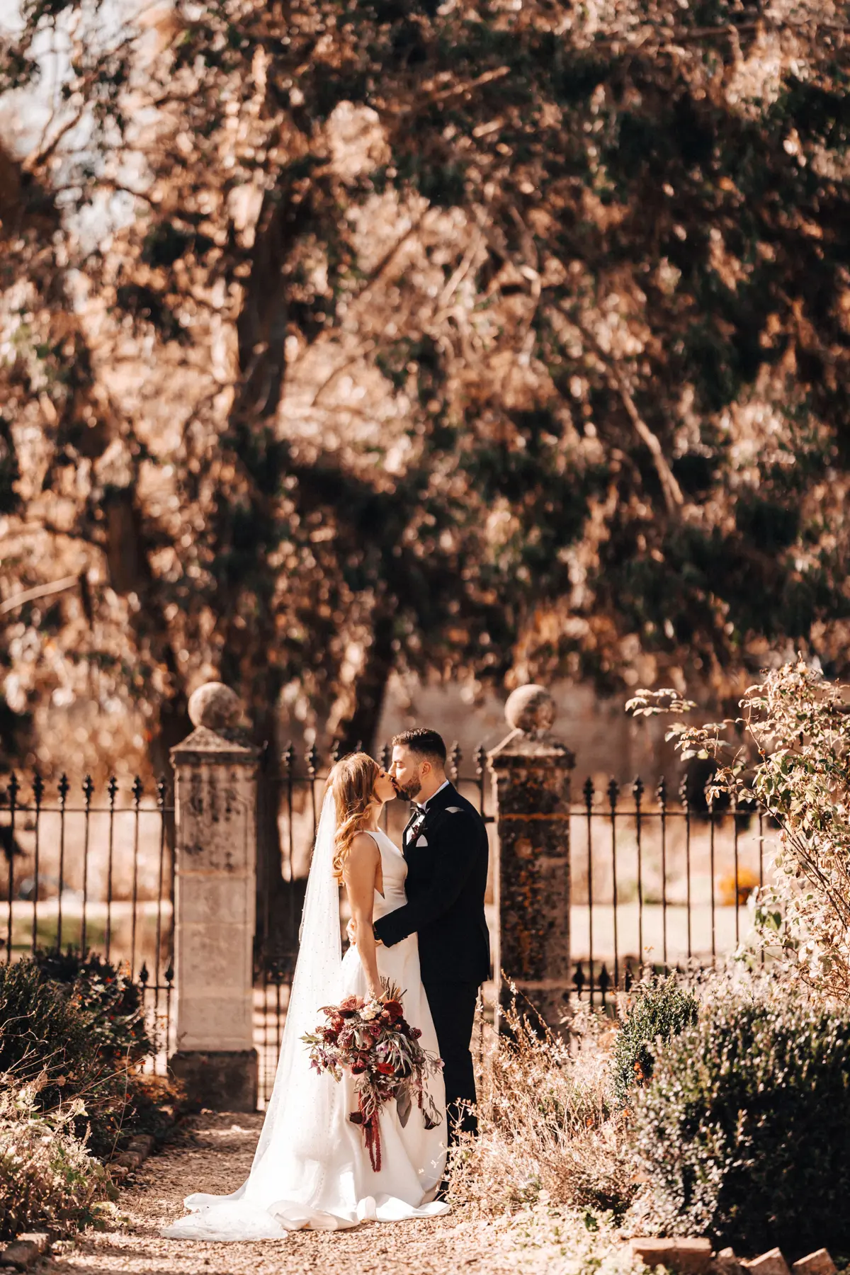 Newlywed couple kiss in autumn walled gardens of Gloucestershire wedding venue elmroe court