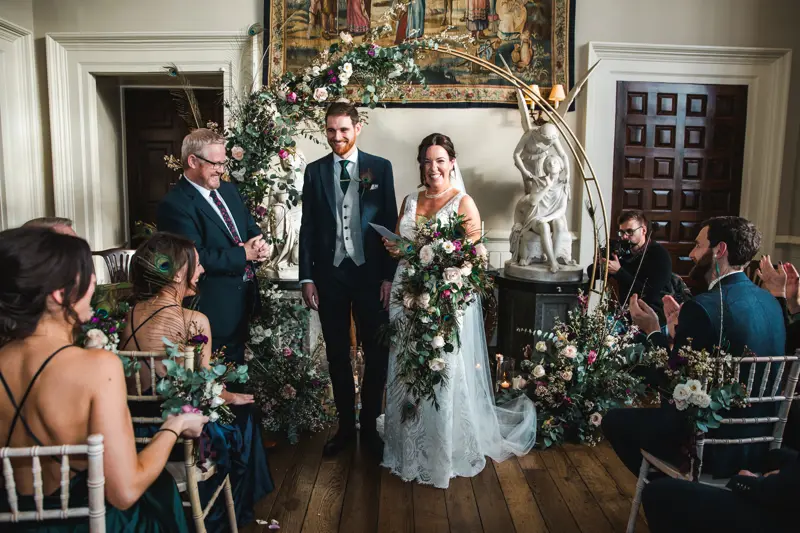 Newlyweds stand in front of beautiful floral decor and bride holds oversized trailing wedding bouquet