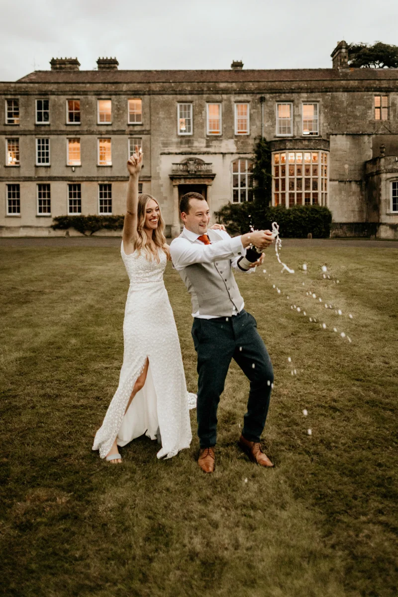 bride and groom celebrating their nuptials with champagne in front of a stately home in Gloucestershire