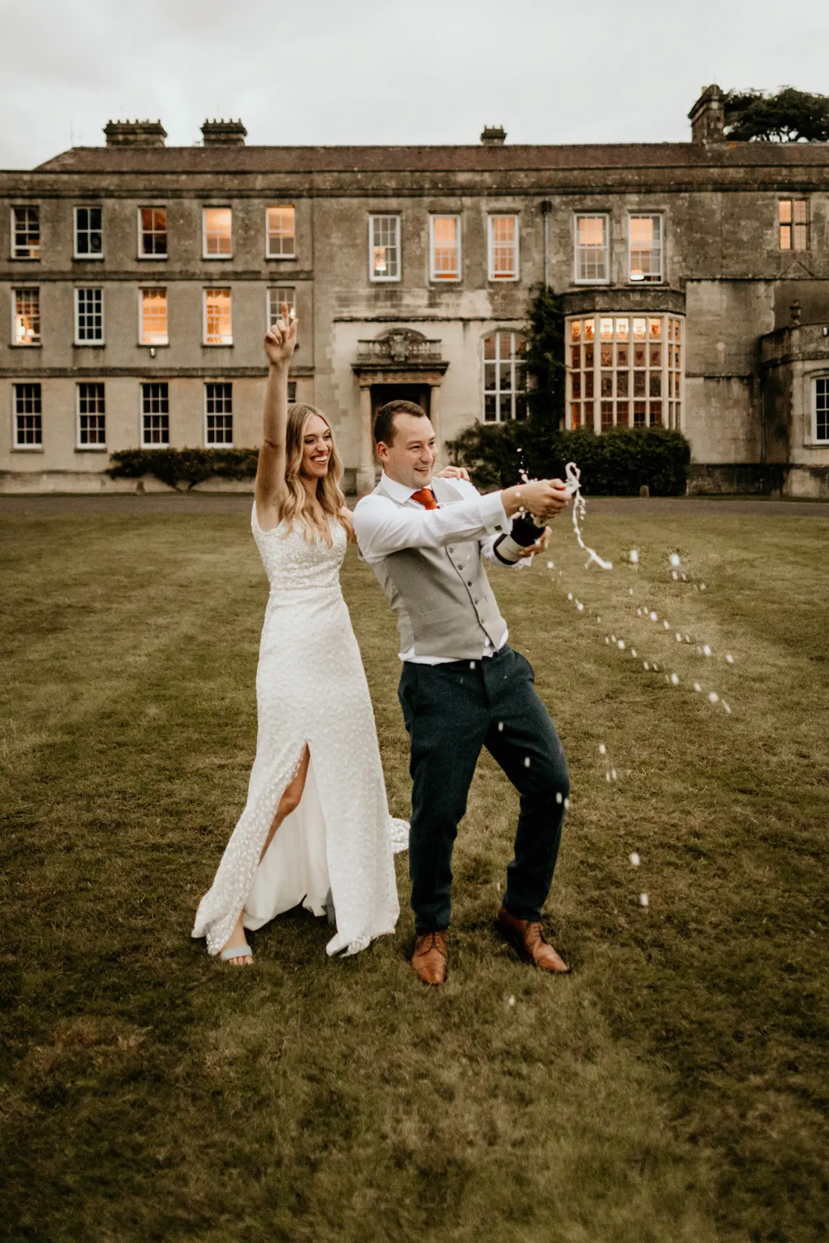 bride and groom celebrating their nuptials with champagne in front of a stately home in Gloucestershire