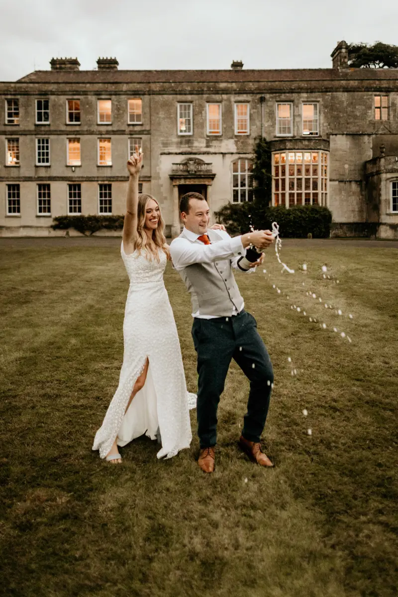bride and groom celebrating their nuptials with champagne in front of a stately home in Gloucestershire