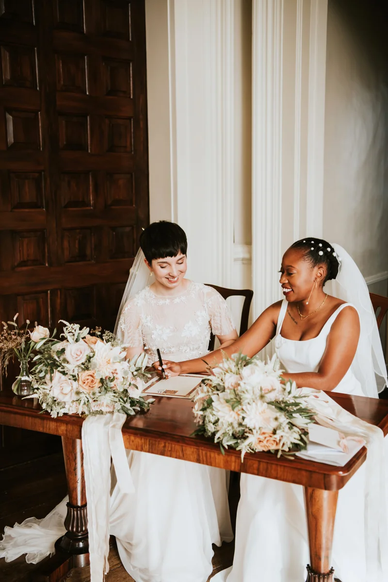 Two brides signing register after their wedding ceremony in stately home in Gloucestershire