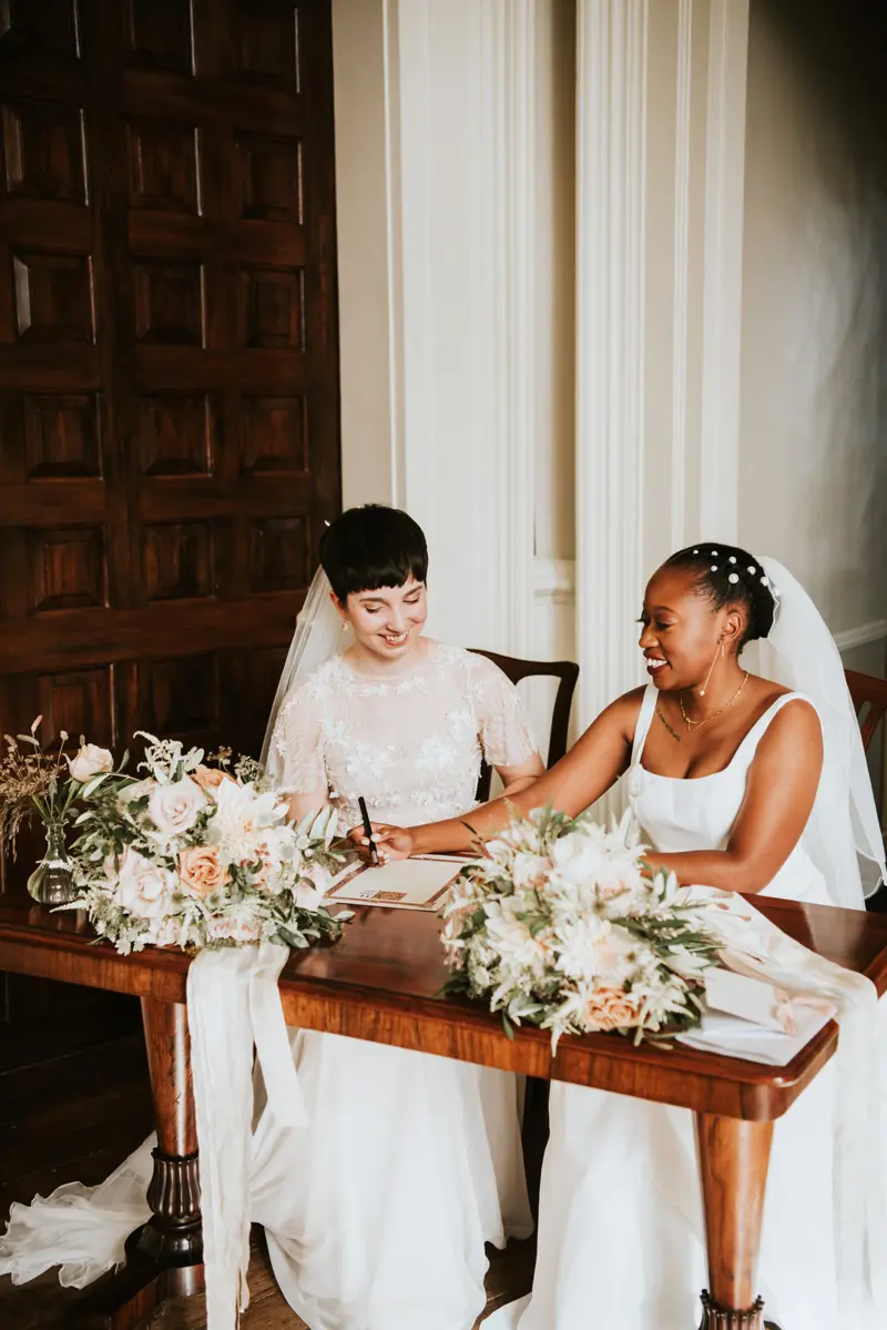 Two brides signing register after their wedding ceremony in stately home in Gloucestershire