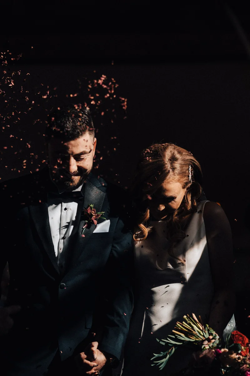 Moody photo of bride and groom confetti being thrown at faces in atmospheric october wedding