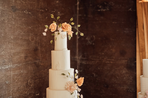 Elegant wedding cake in front of the rammed earth wall of eco wedding reception venue at Elmore Court in Gloucestershire