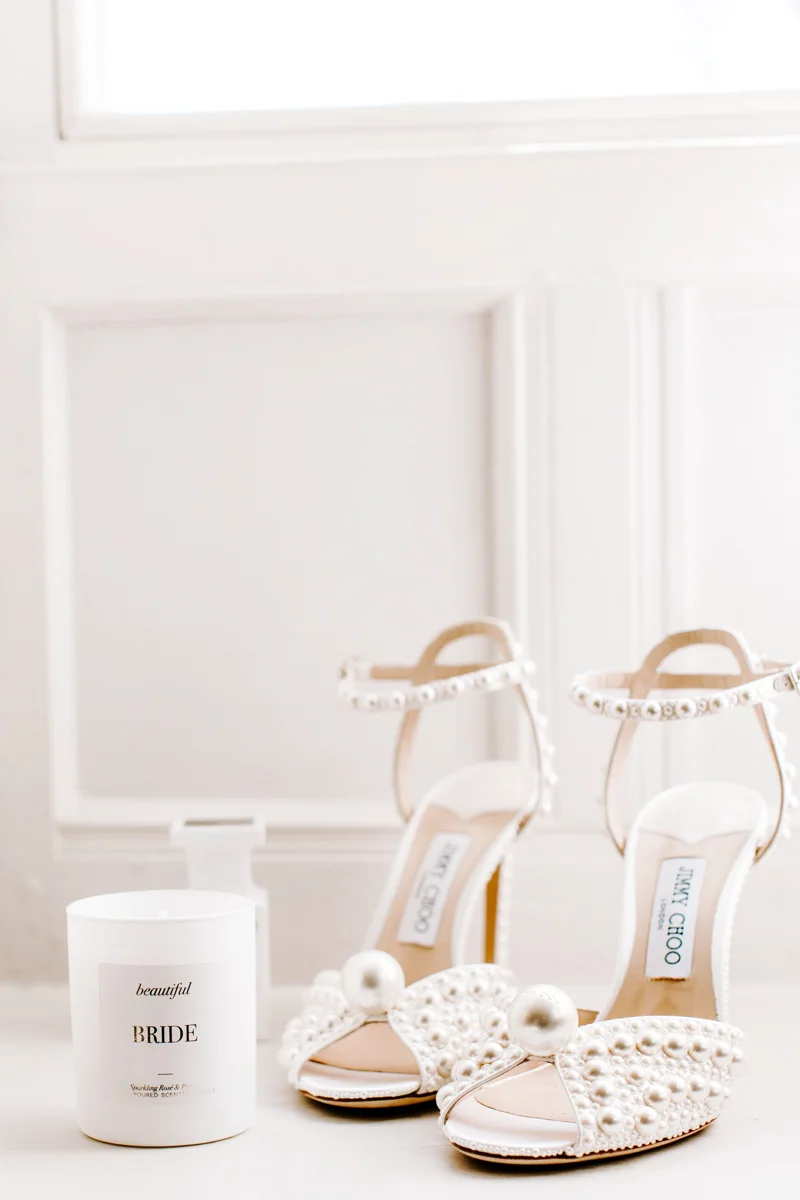 Glamorous Jimmy choo pearl bridal heels with all over pearls and large pearl on toe next to bridal candle on white wooden windowsill