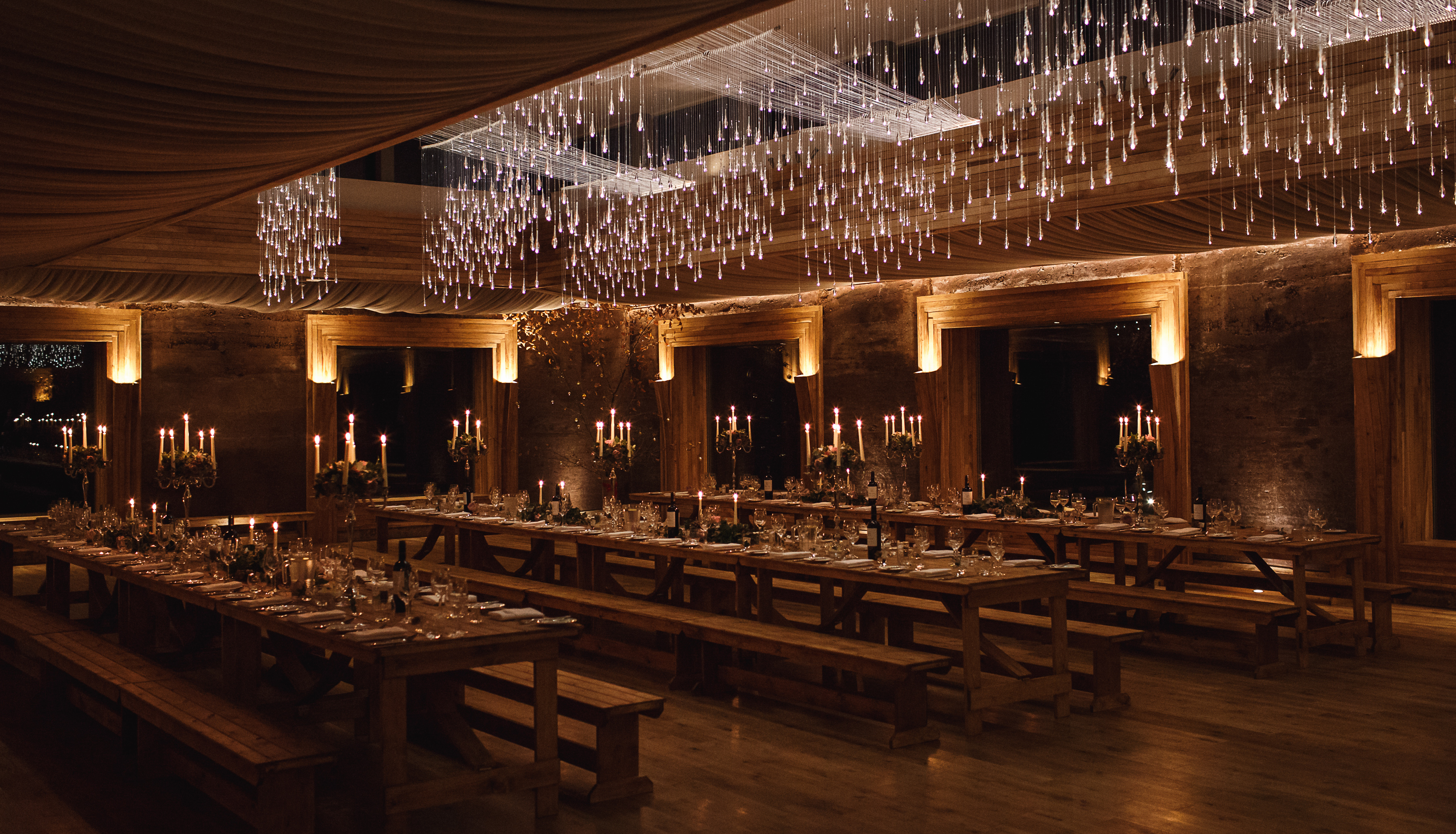 A candlelit wedding banquet laid ready in the dimly lit Gillyflower, an eco wedding venue at Elmore Court in Gloucester