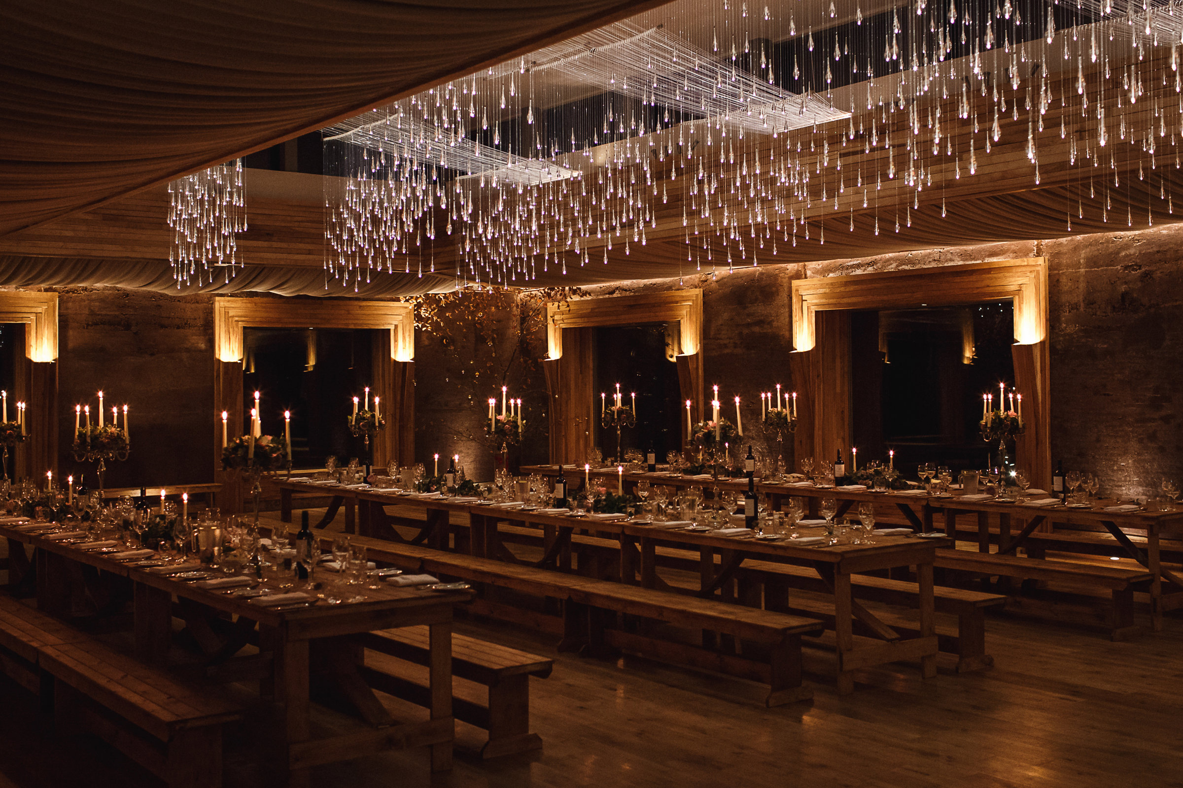 A candlelit wedding banquet laid ready in the dimly lit Gillyflower, an eco wedding venue at Elmore Court in Gloucester