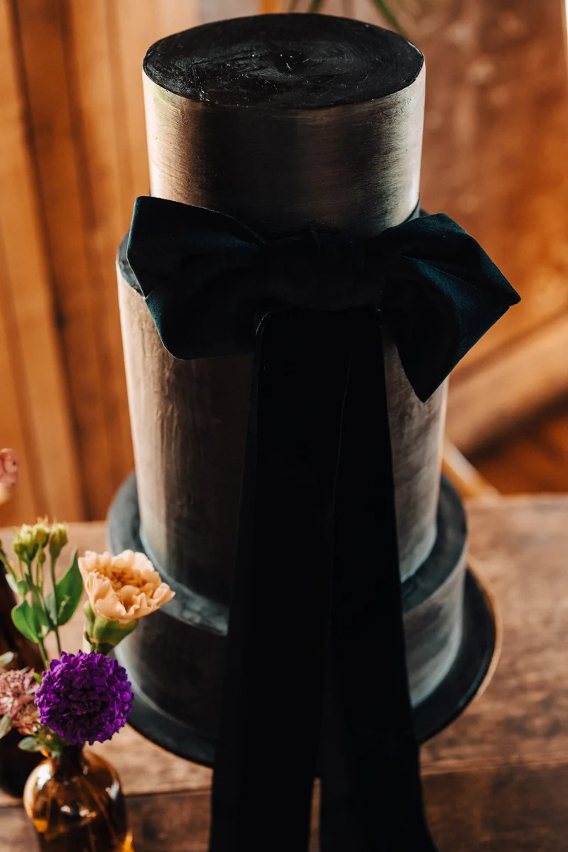 This Black wedding cake with velvet ribbon was handmade by the bride herself for her magical moody wedding with dark details at a mansion house near halloween in october