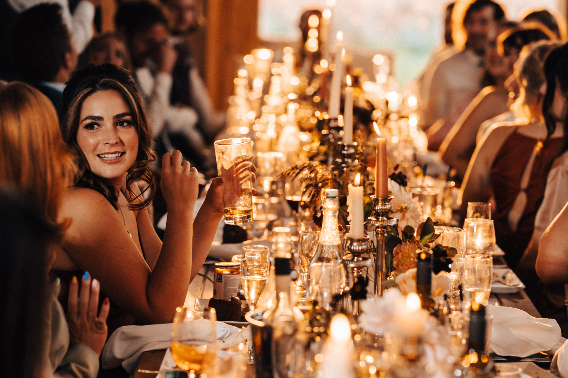 Glowing golden hour September wedding reception with candles on long tables and guests smiling