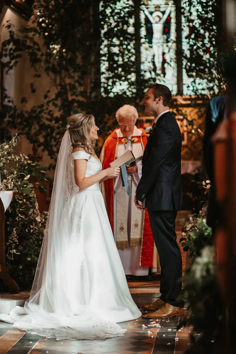 Religious ceremony in church Vicar behind couple who are smiling holding hands in church