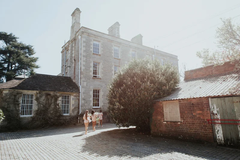 Bridesmaids in pyjamas walking towards Stately home Elmore Court in the hazy spring sunshine