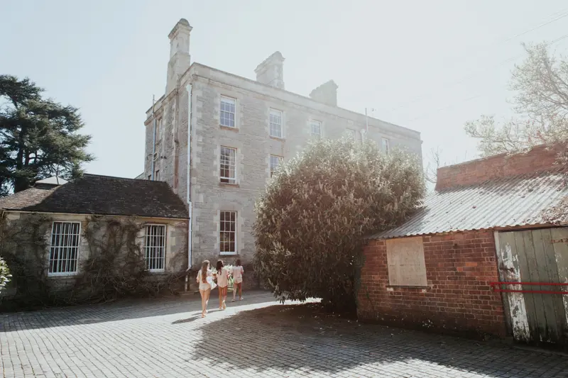 Bridesmaids in pyjamas walking towards Stately home Elmore Court in the hazy spring sunshine