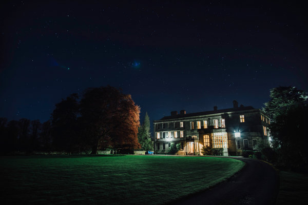 Glowing stately home Elmore Court at night. The huge beech tree to the left of the grade two listed house is slightly lit up by the light from the windows