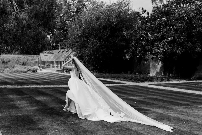 bride in long romantic veil walking through a walled garden of a stately home in gloucsteshire