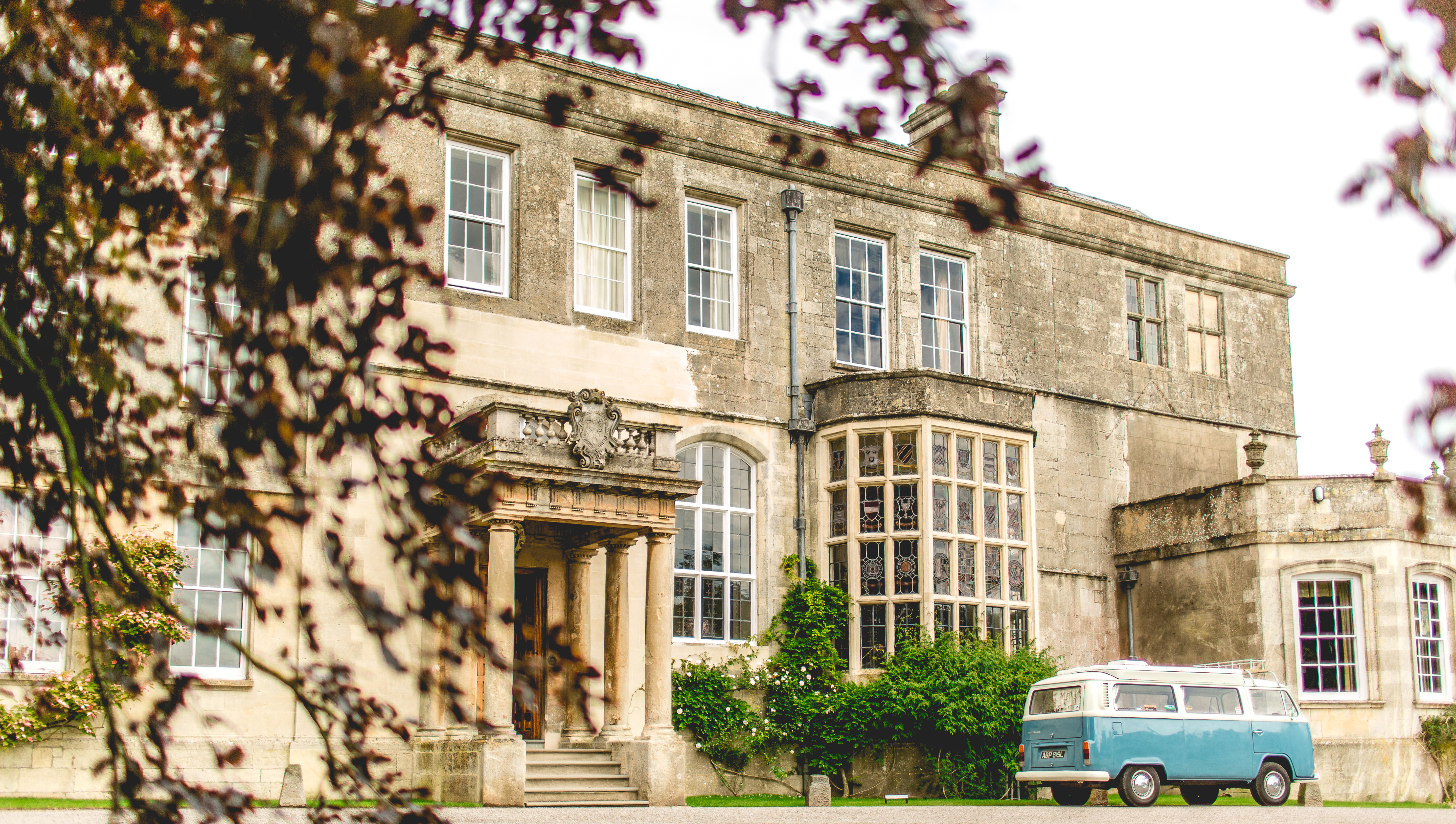 Stately home Elmore Court with a blue VW camper parked outside and copper beech in front of the house at a wedding