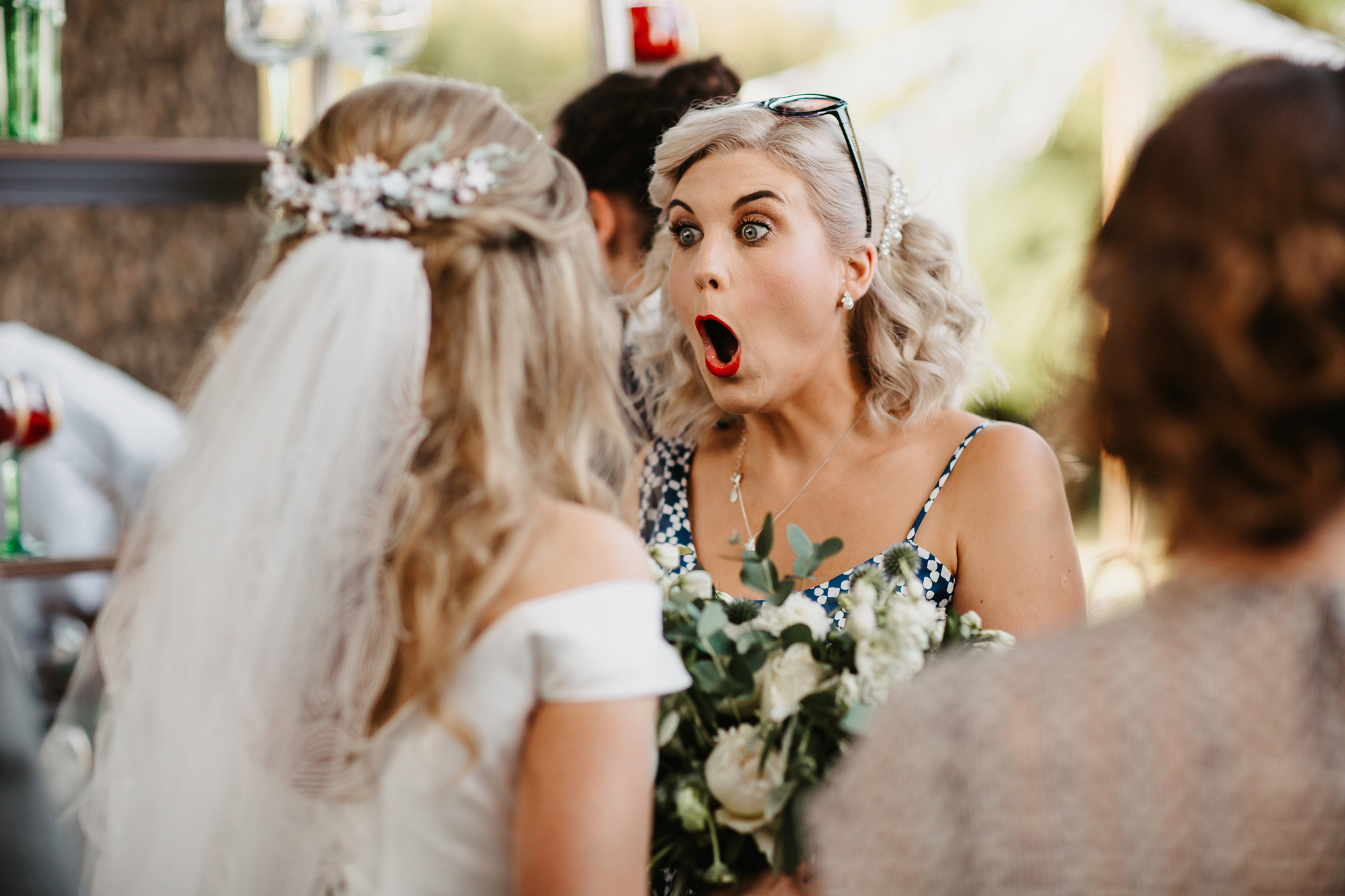 A female wedding guest pulls a funny shocked face at the bride