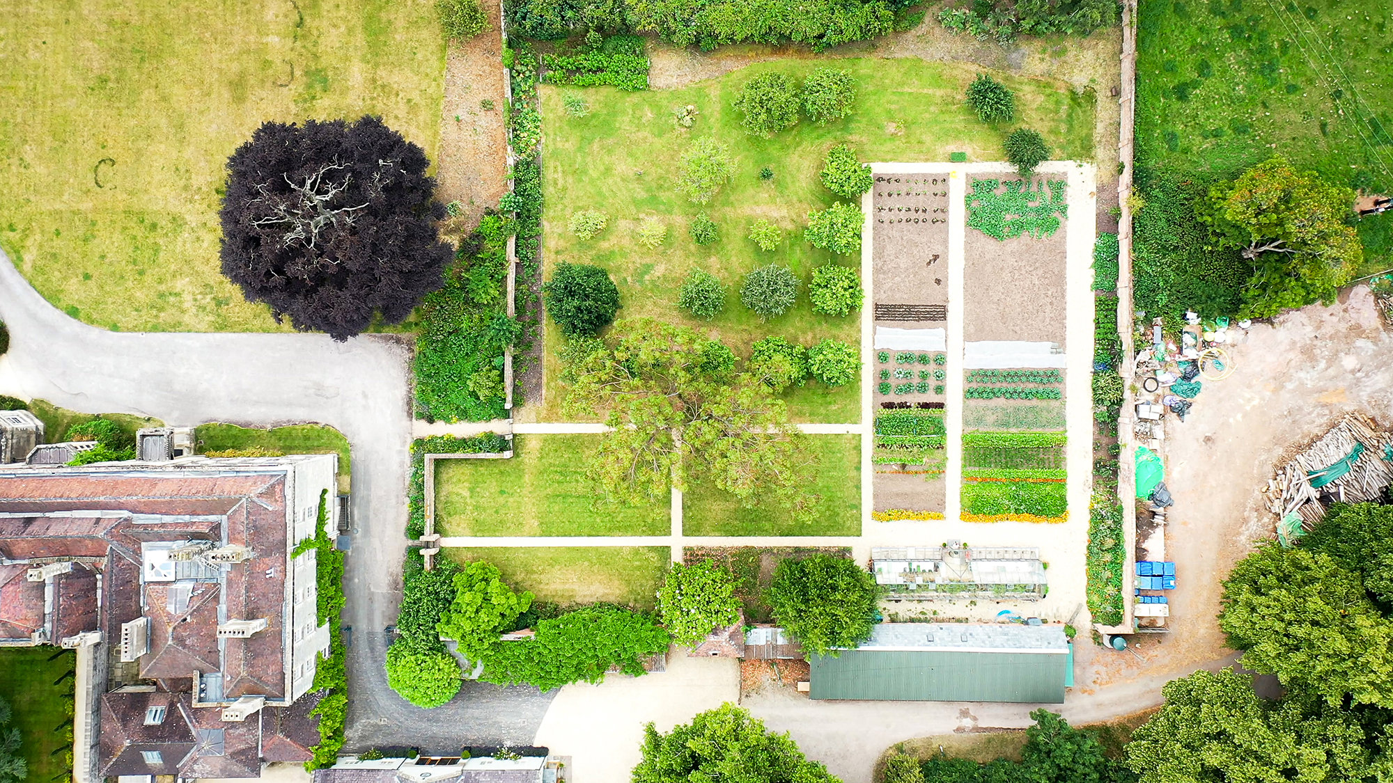 Ariel view of a kitchen garden full of vegetables, a greenhouse and a small orchard of fruit trees
