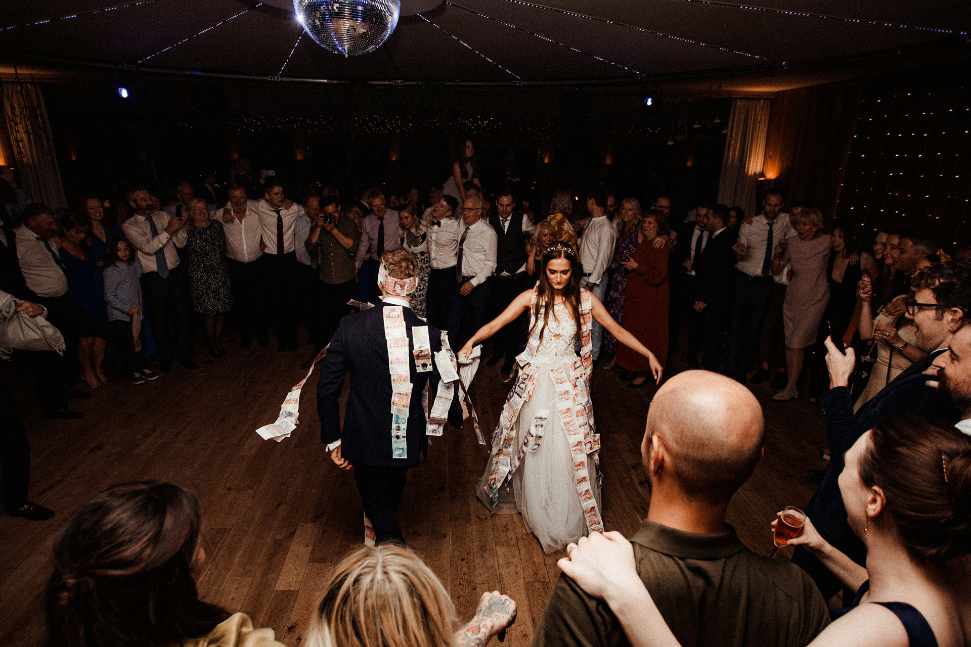 Bride and Groom dance in centre of guests covered in money during their Greek money dance party wedding